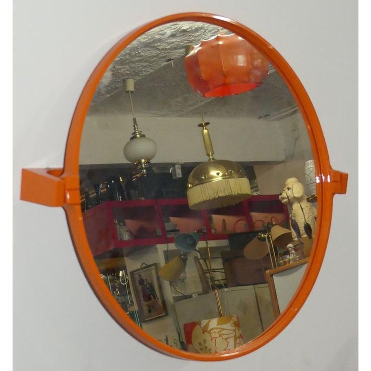 an orange circular mirror hanging on the side of a wall next to a shelf filled with lamps