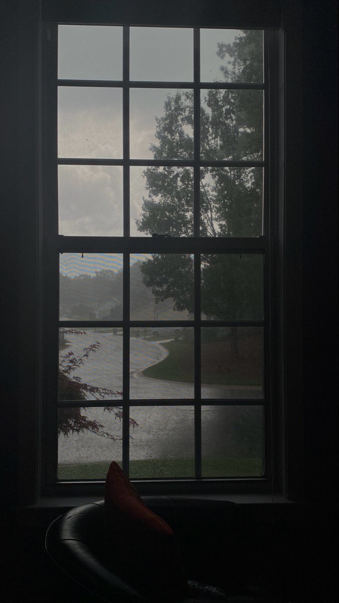 an open window in a dark room looking out at a lake and trees on the other side