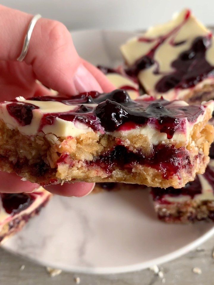 someone is holding up some dessert on a plate with white chocolate and blueberry toppings