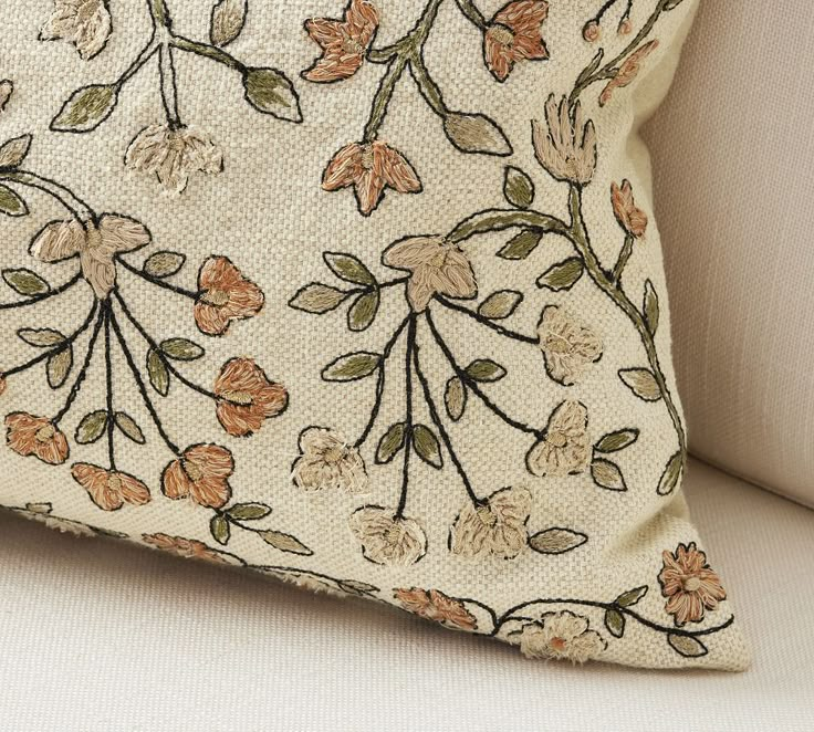 a close up of a pillow on a couch with flowers and leaves embroidered on it