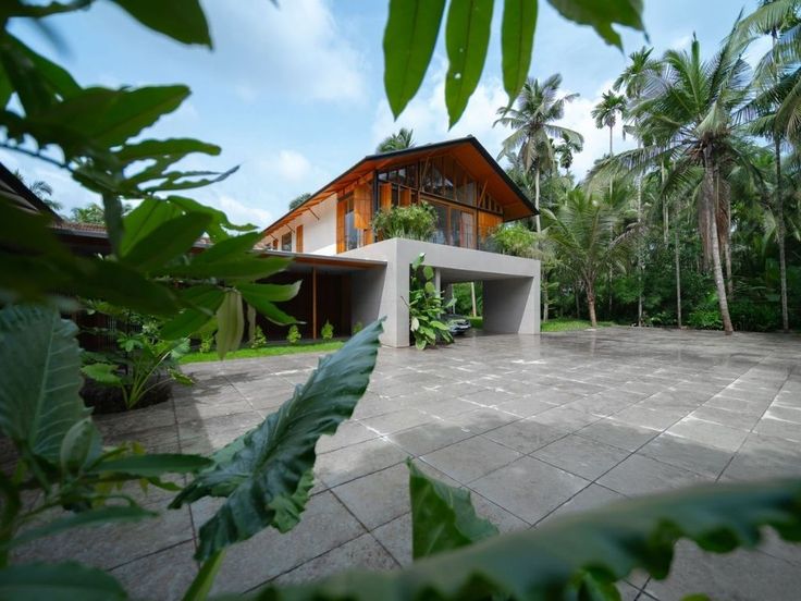 the house is surrounded by lush vegetation and palm trees, with an open patio area