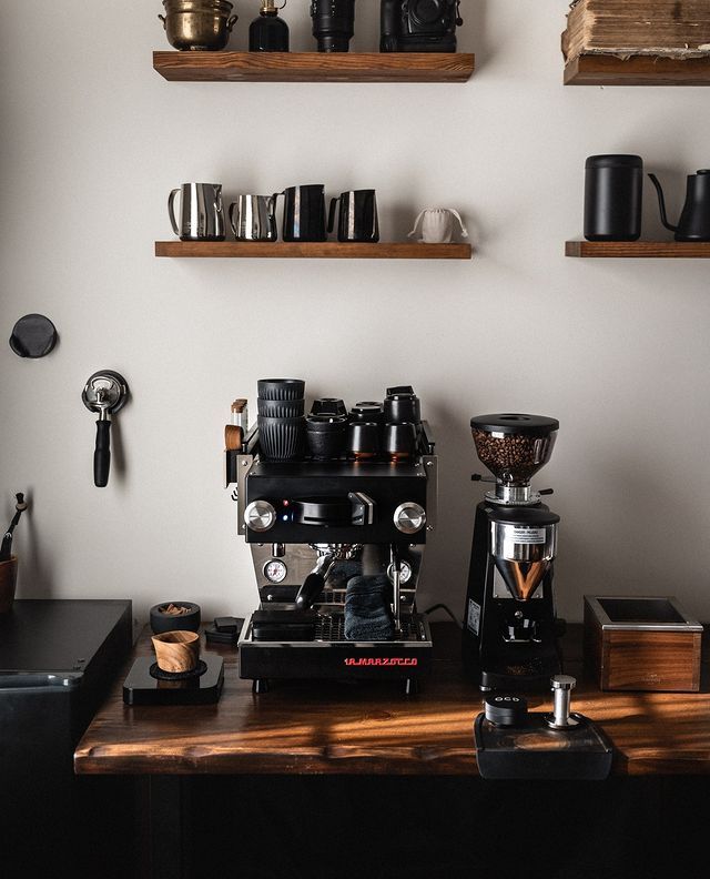 a coffee machine sitting on top of a wooden table next to shelves filled with cups