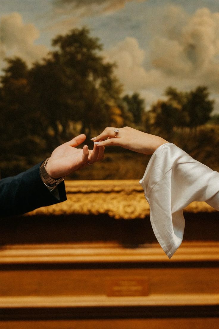 two people reaching out their hands to each other in front of a painting with trees