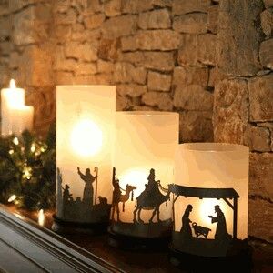 three lit candles sitting on top of a mantle filled with nativity scene silhouettes