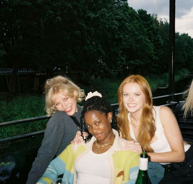 three women standing next to each other in front of trees