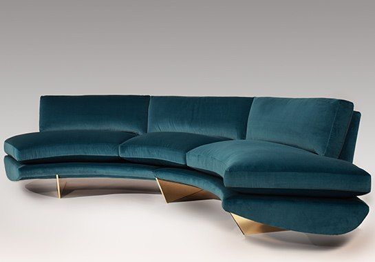 a blue sectional couch with gold legs on a white floor