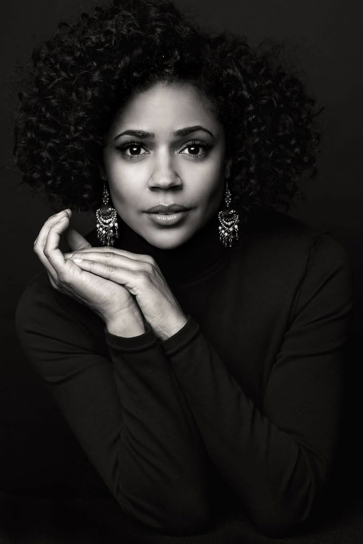 a black and white photo of a woman with her hand on her chin, looking at the camera