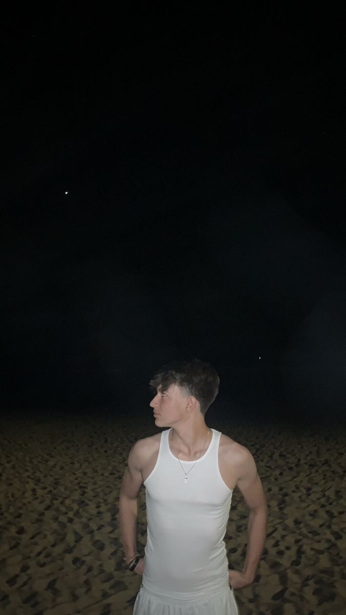 a man standing in the sand at night with his hands on his hips and looking off into the distance