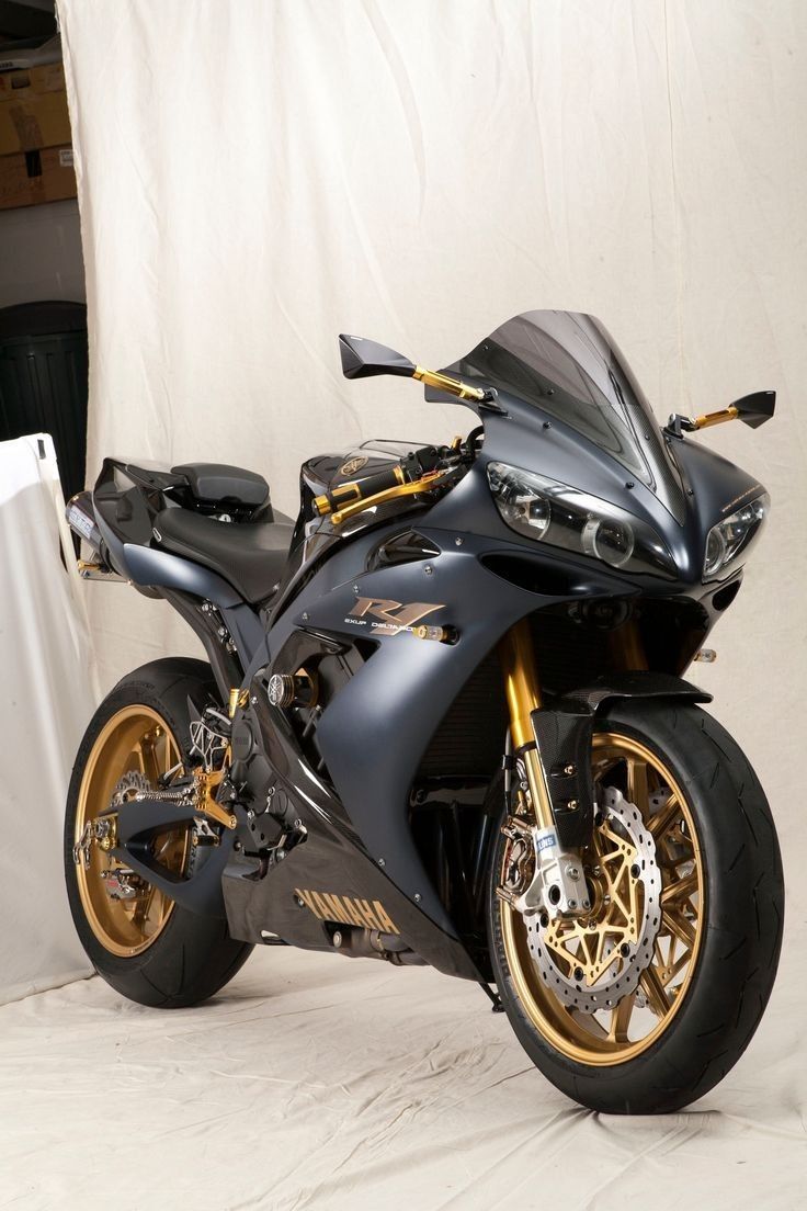 a black and gold motorcycle parked in front of a white wall with curtains behind it