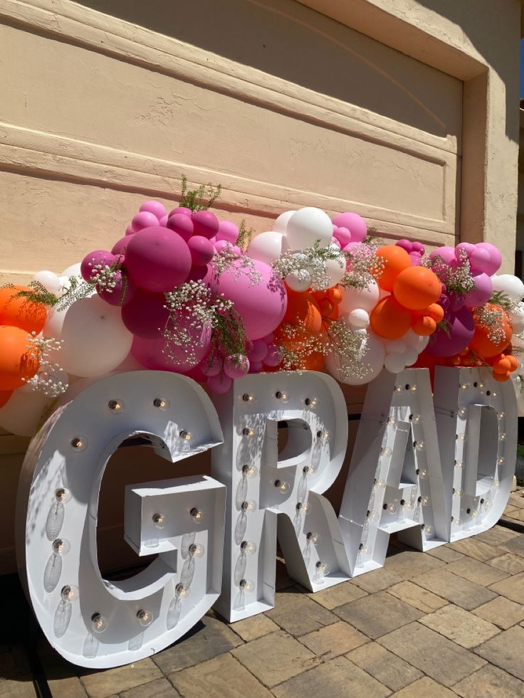 a large sign that says grad with balloons and flowers on it in front of a building