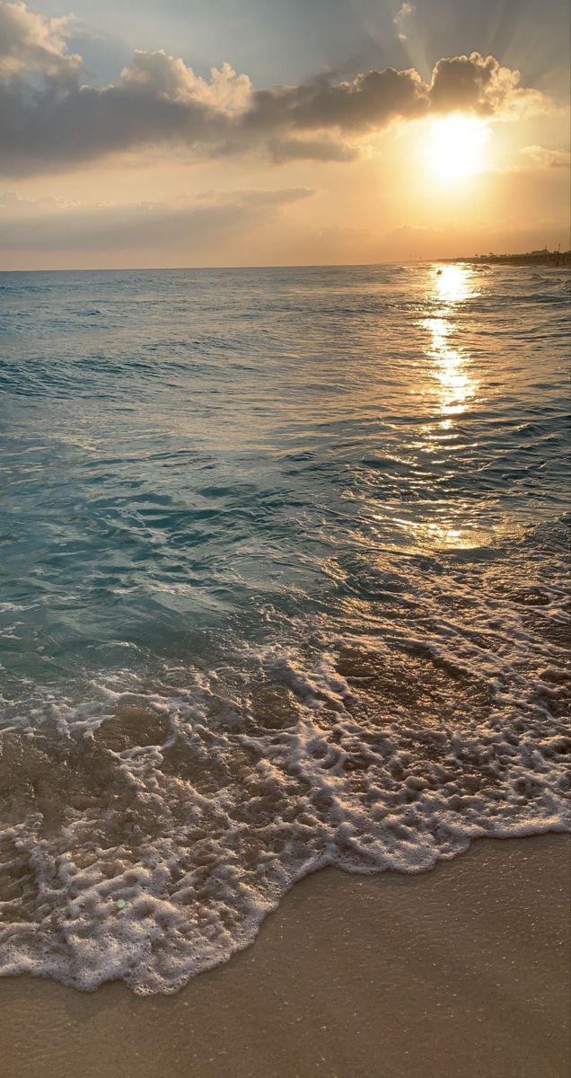 the sun is setting over the ocean with waves crashing on the beach and sand in the foreground