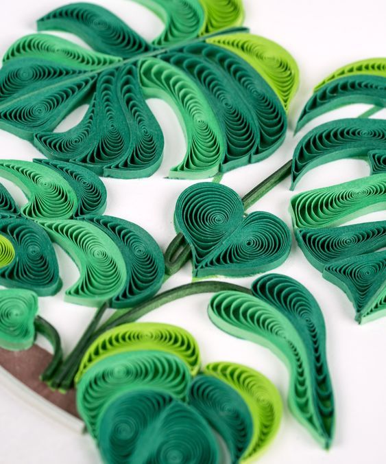 green paper cut flowers on a white surface with scissors in the foreground, and another piece of art that appears to be made out of cardboard