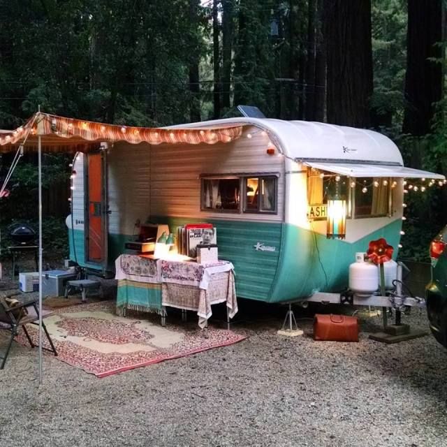 an rv is parked in the woods with lights strung from it's awnings