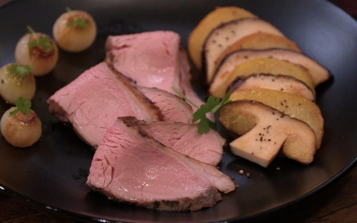 sliced meat and potatoes on a black plate