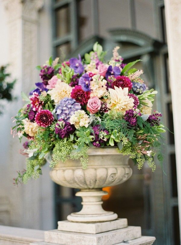 a vase filled with lots of flowers sitting on top of a stone step next to a building