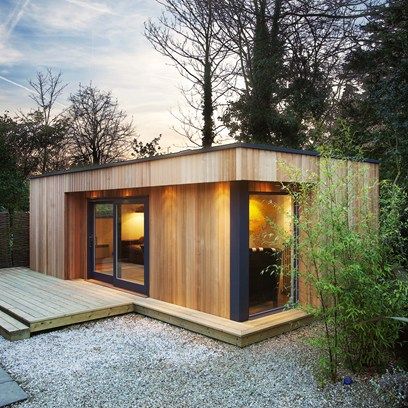 a small wooden building sitting on top of a gravel field next to a lush green forest