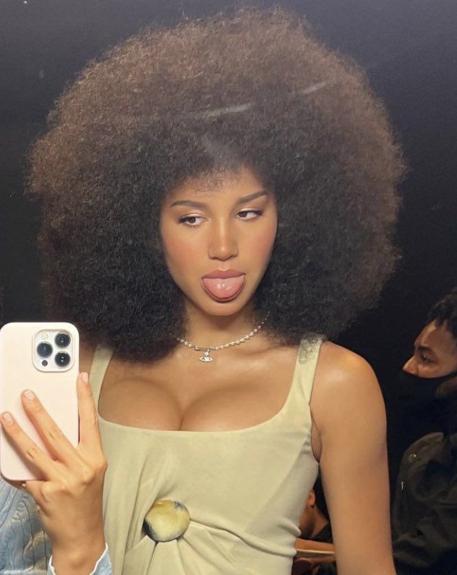 a woman taking a selfie with her cell phone in front of her face and an afro wig on