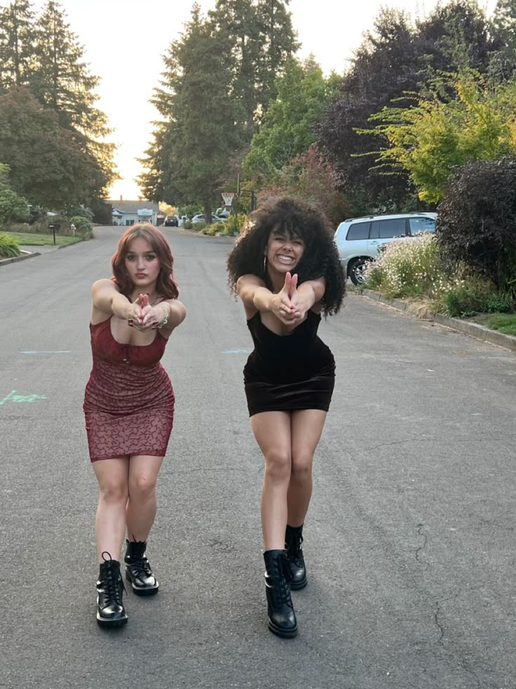 two women are standing on the street pointing their fingers at something in front of them