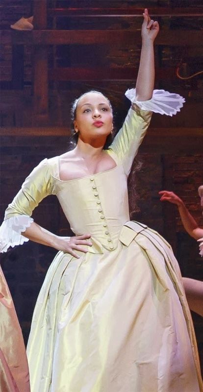 a woman in a white dress standing next to another woman wearing a yellow dress and holding her hand up