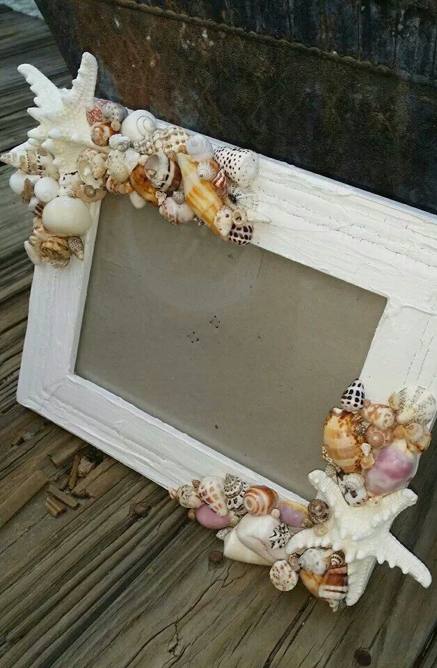 an old white frame with sea shells and seashells on the bottom is sitting on a wooden floor