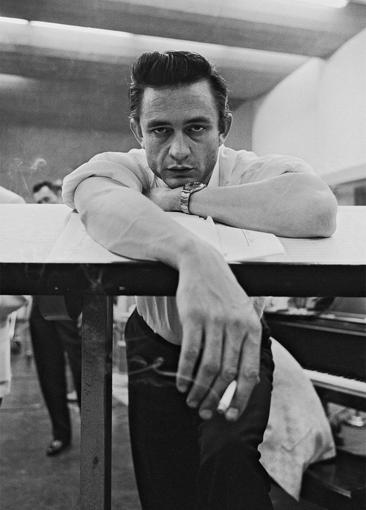 a black and white photo of a man leaning on a table with his arms crossed