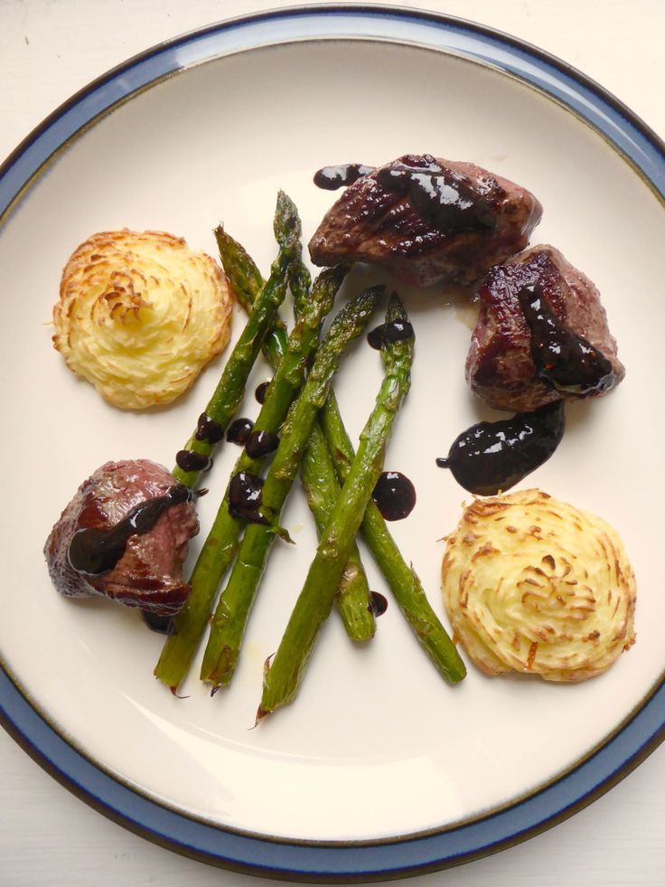 a white plate topped with meat and asparagus