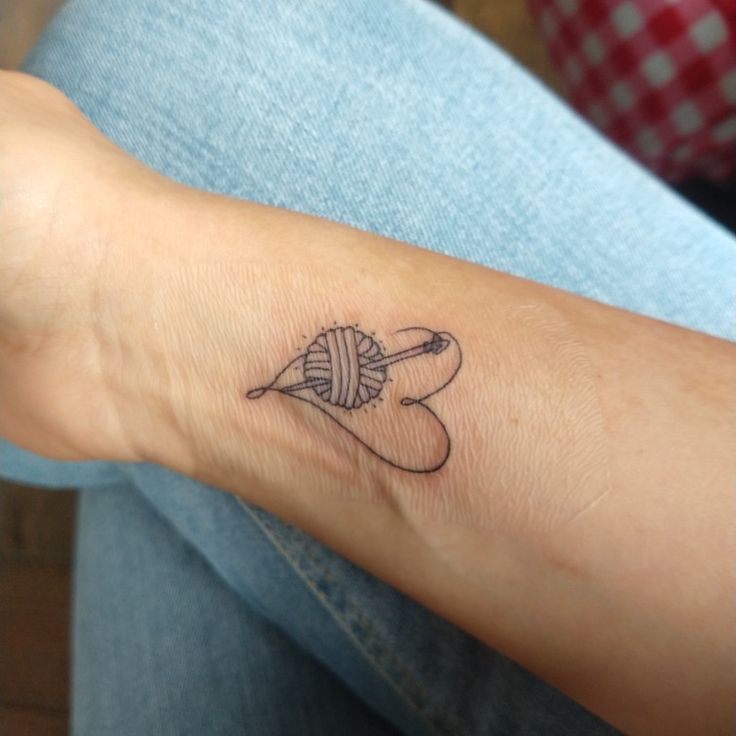 a person with a tattoo on their arm holding a ball of yarn and knitting needles