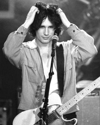 a young man holding his head while standing in front of a microphone with an electric guitar