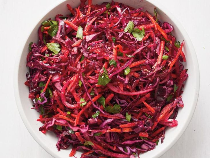 a white bowl filled with red cabbage and green leafy garnish on top of a table