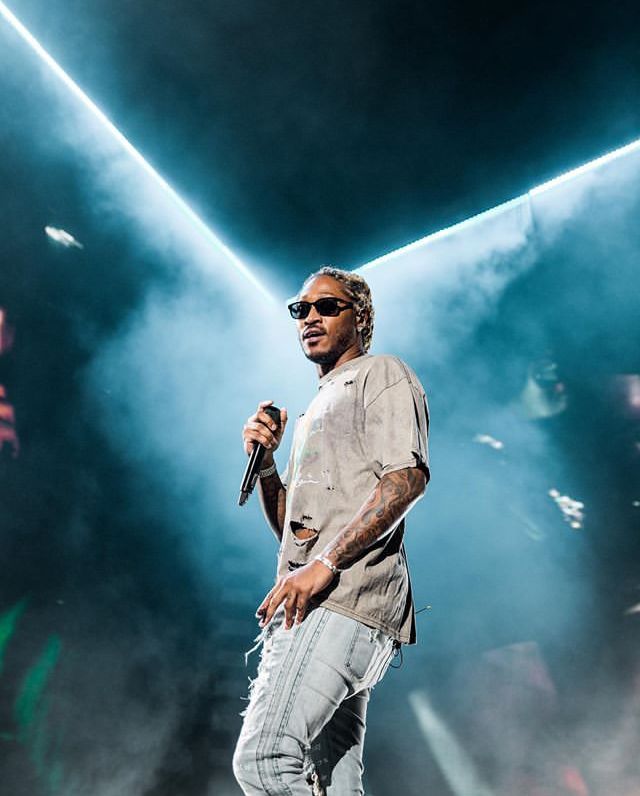 a man standing on top of a stage holding a microphone in his hand and wearing sunglasses