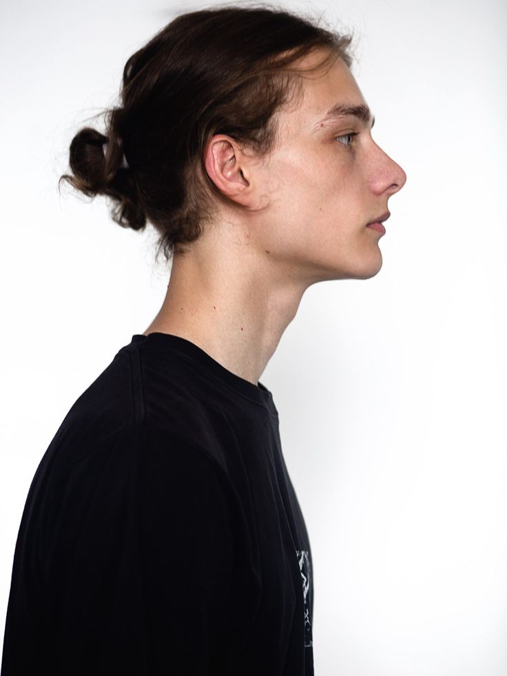 a young woman with a messy topknott looks off to the side while wearing a black t - shirt