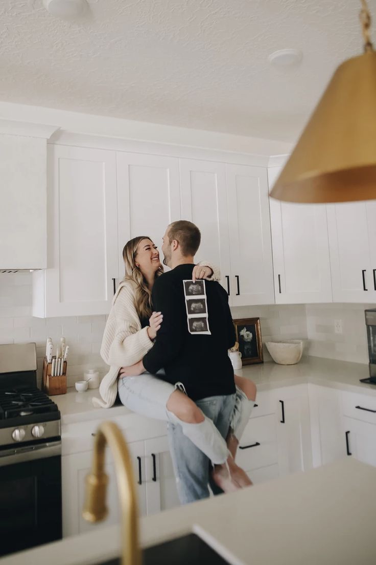 a man and woman sitting on top of a kitchen counter next to each other in front of an oven