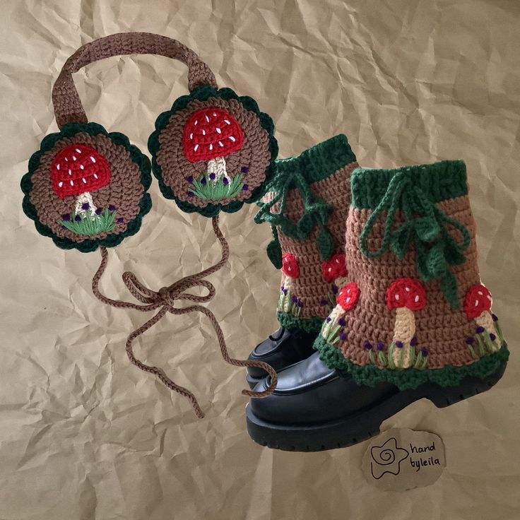 two crocheted boots with flower and mushroom decorations on them, one has a string attached to it