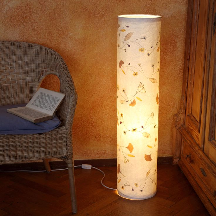 a lamp that is sitting on the floor next to a wicker chair and a book