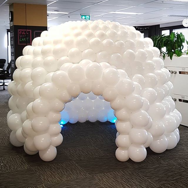 an arch made out of white balloons in an office cubicle with desks and chairs