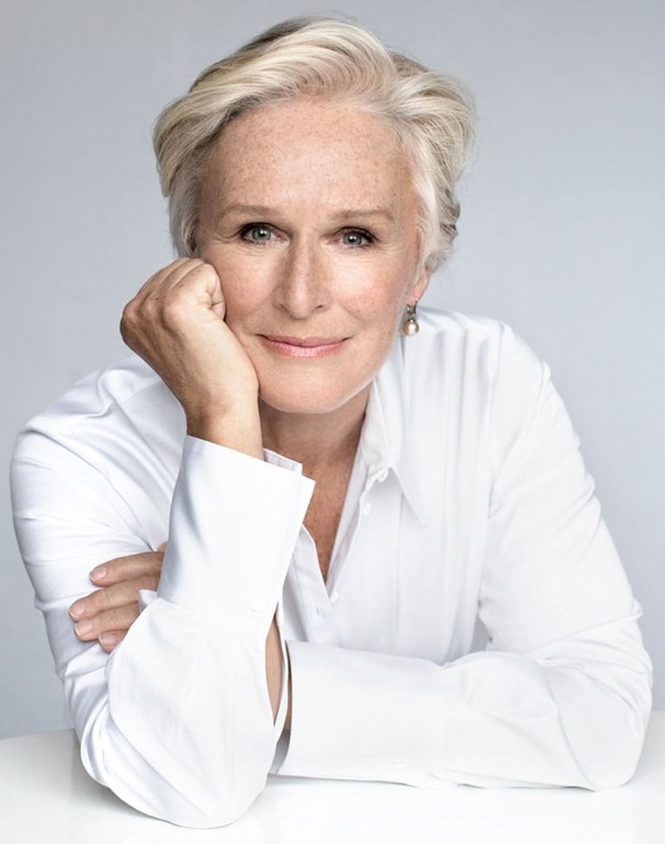 an older woman sitting at a table with her hand on her chin and looking into the camera