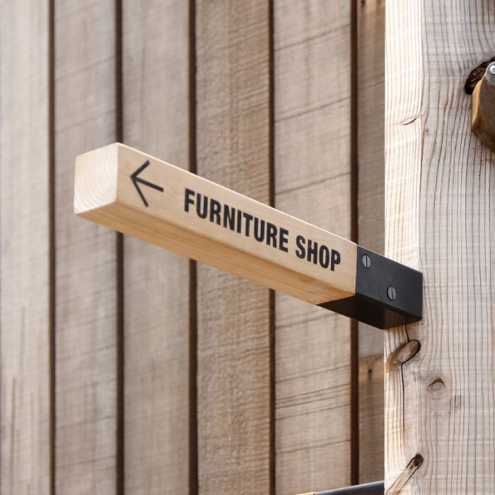 a wooden sign that says furniture shop hanging from the side of a building with an arrow pointing to it