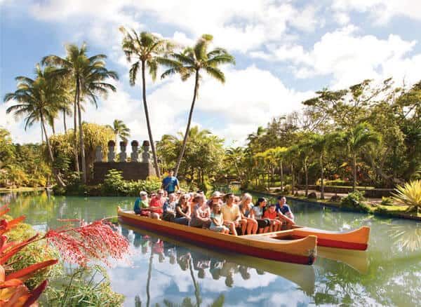 a group of people riding on the back of a boat down a river surrounded by palm trees