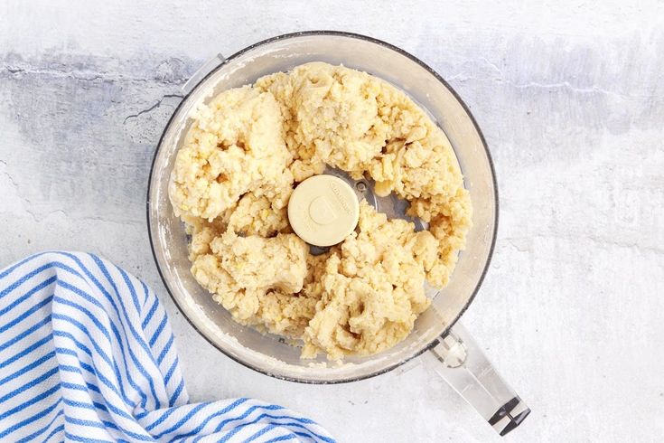 a food processor filled with dough on top of a blue and white striped towel next to it