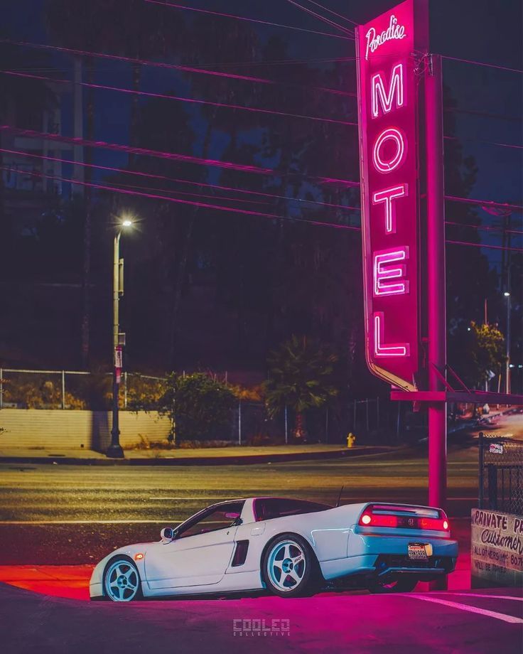 a white sports car parked in front of a motel sign at night with the lights on