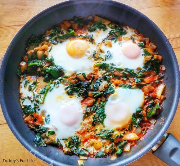 two fried eggs in a skillet with spinach and other vegetables on the side