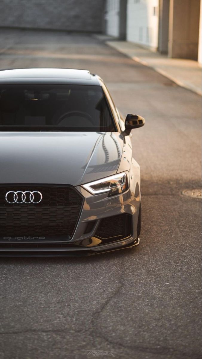 the front end of a gray car parked in a parking lot next to a building