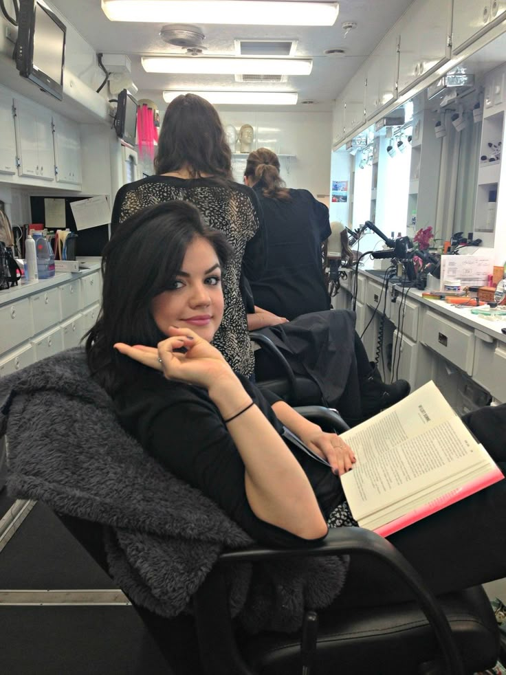 a woman sitting in a hair salon chair reading a book and pointing at the camera