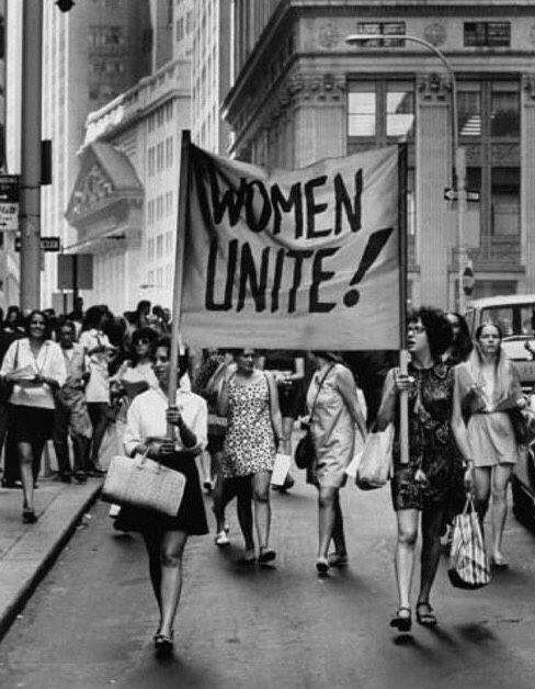 black and white photograph of women marching down the street holding signs that read women united