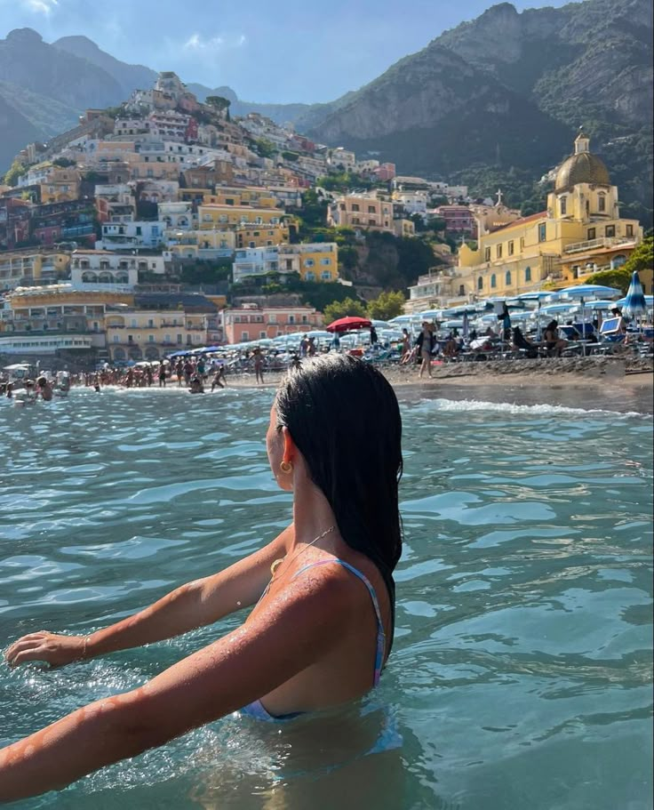 a woman sitting in the ocean with her arms out and looking at the beach below