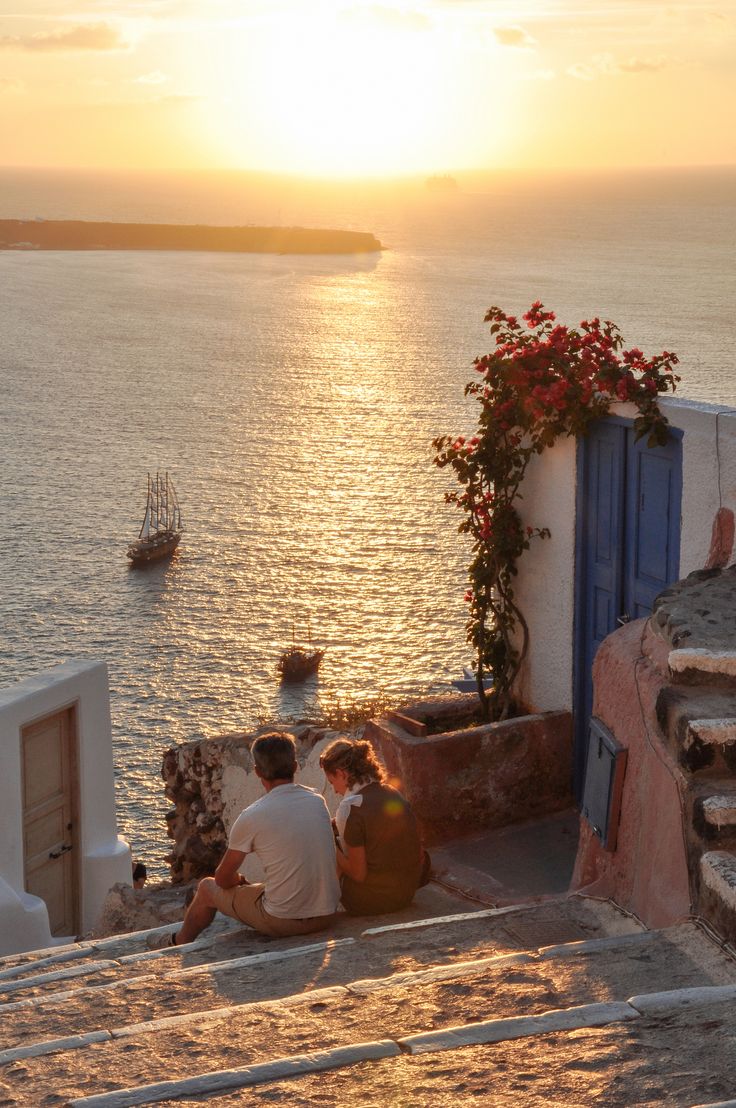 the sun is setting over the ocean and some people are sitting on benches near the water