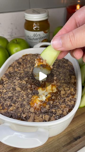 a person dipping an apple into a casserole dish