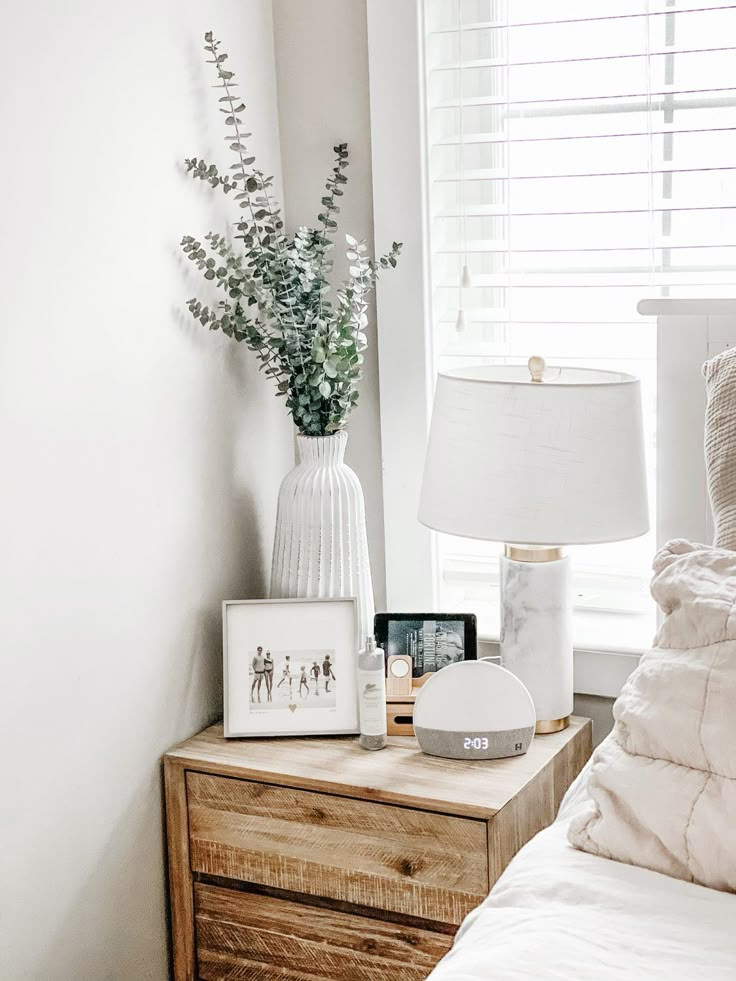 a bedroom with a bed, nightstand and lamp on it's night stand in front of a window