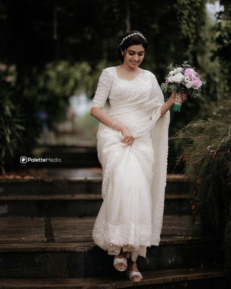 a woman in a white dress is walking down some steps with flowers and a bouquet