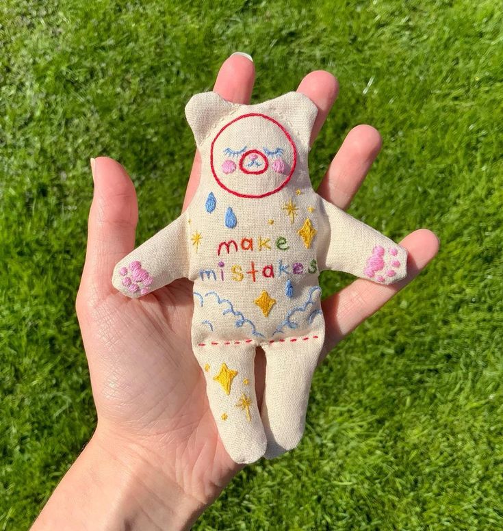 a hand holding a small stuffed animal on top of a green grass covered field,